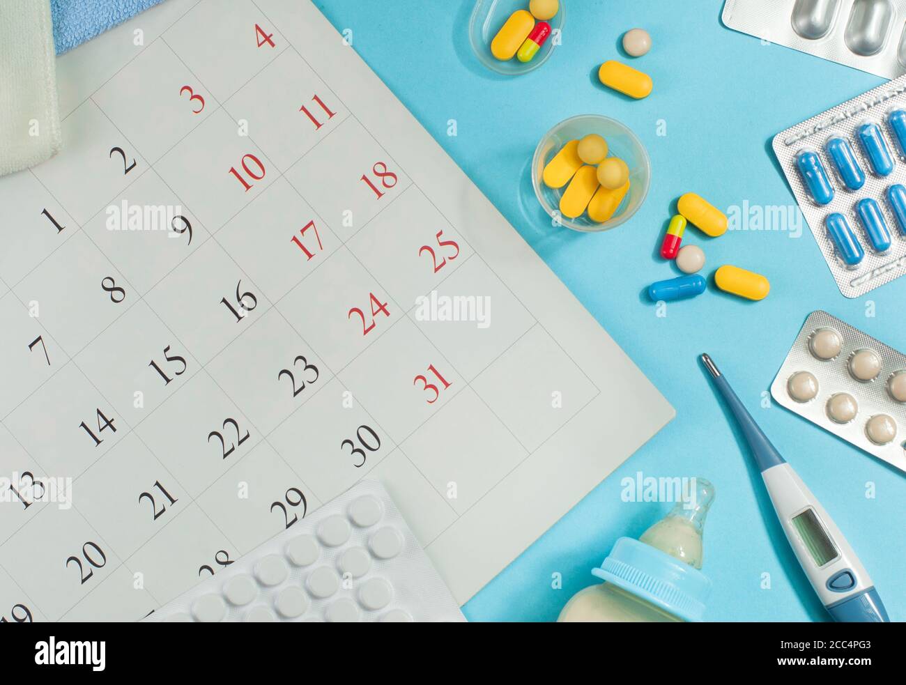 Capsule pills, milk bottle and electronic thermometer near calendar page Stock Photo