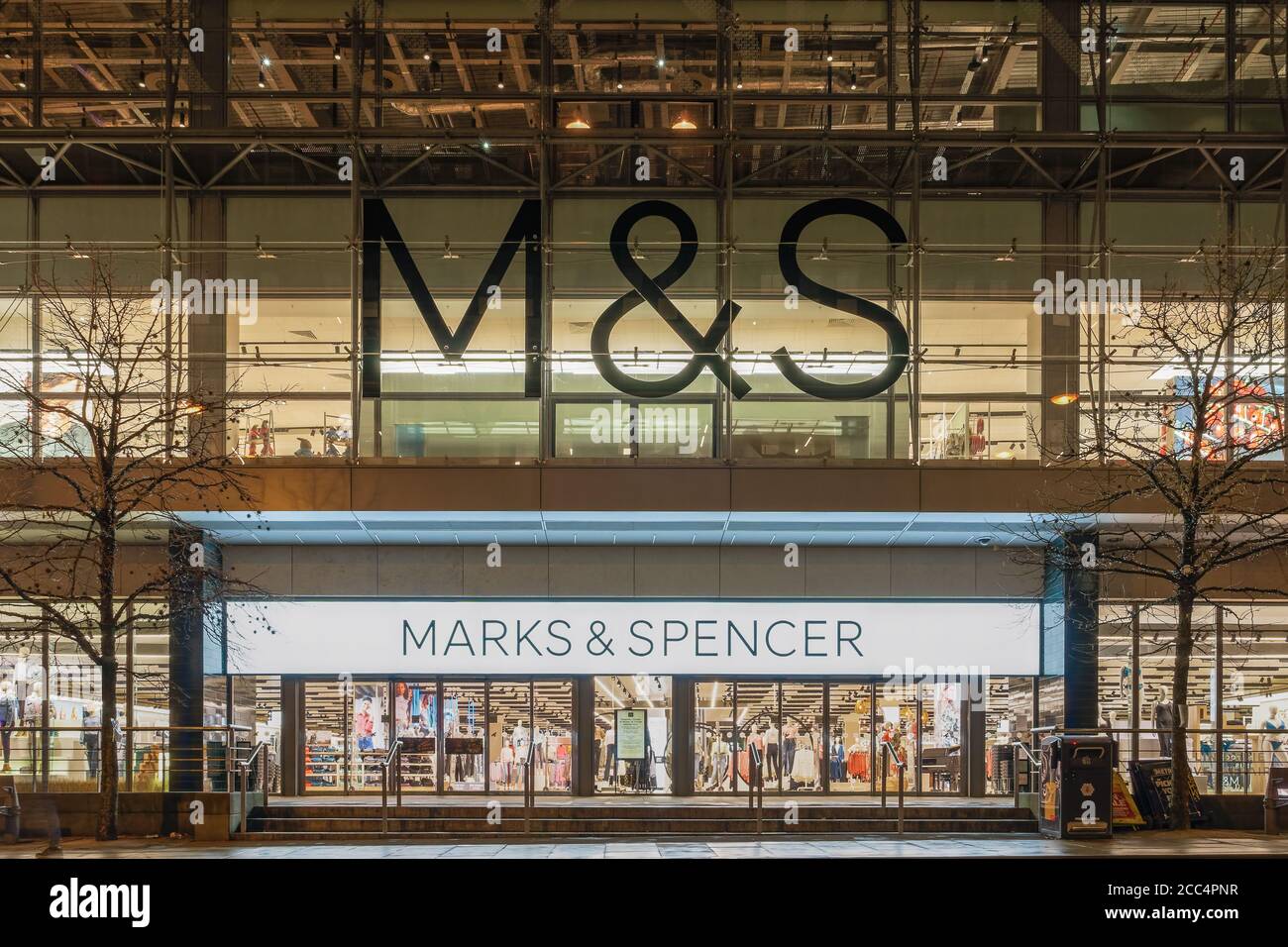 Manchester, UK Marks & Spencer store facade with logo. Illuminated night view of British retailer M&S Group plc closed shop entrance with logo & sign. Stock Photo