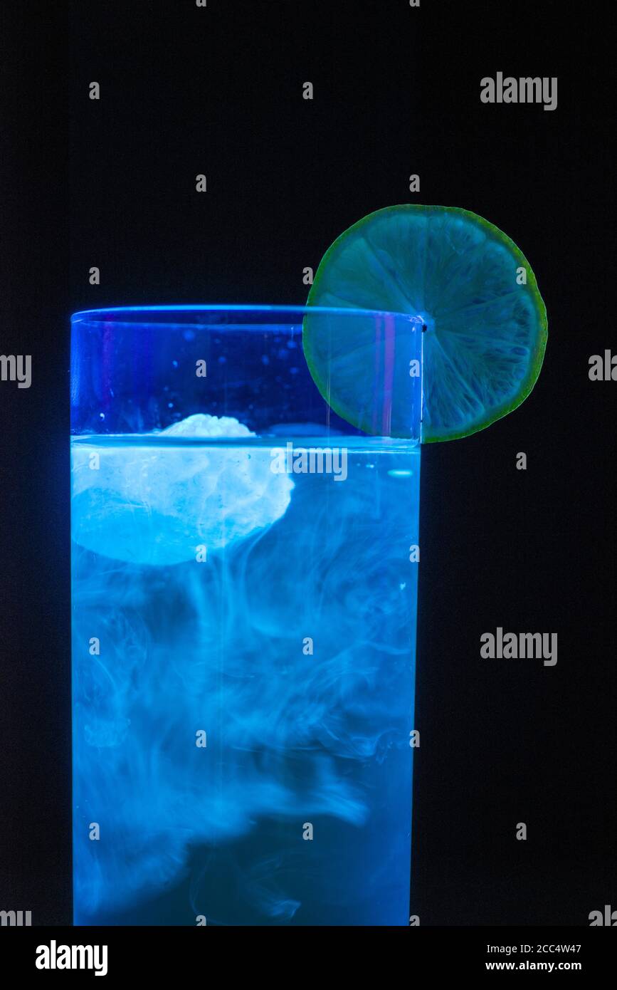 Gin with ice cube made from tonic water containing quinine, fluorescing in ultraviolet light Stock Photo