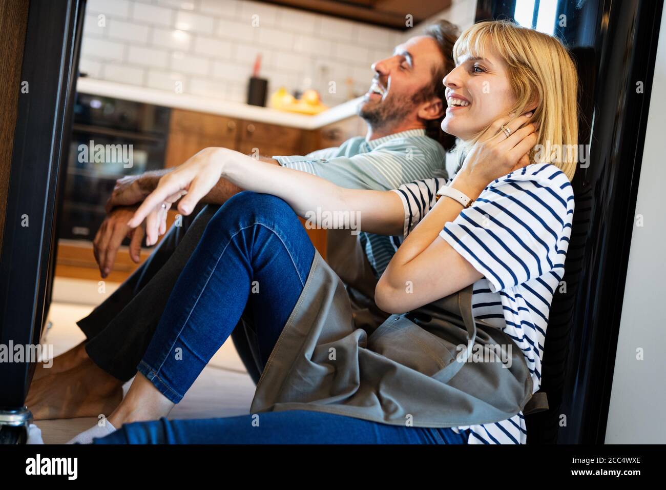 Young happy tired couple sitting on kitchen floor after cooking Stock Photo