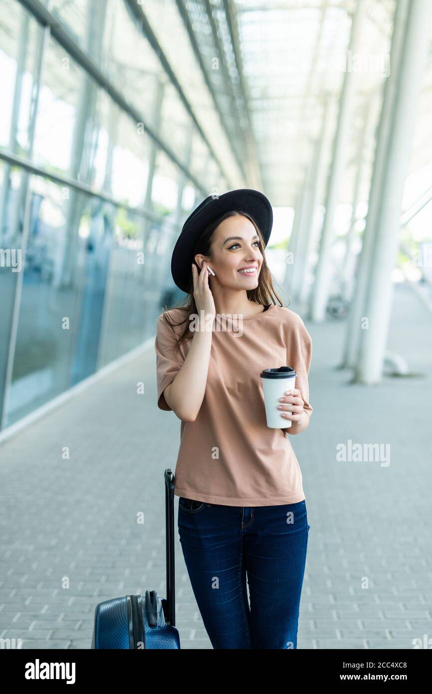 Young woman carry baggage speak via airpods with phone in hands walking