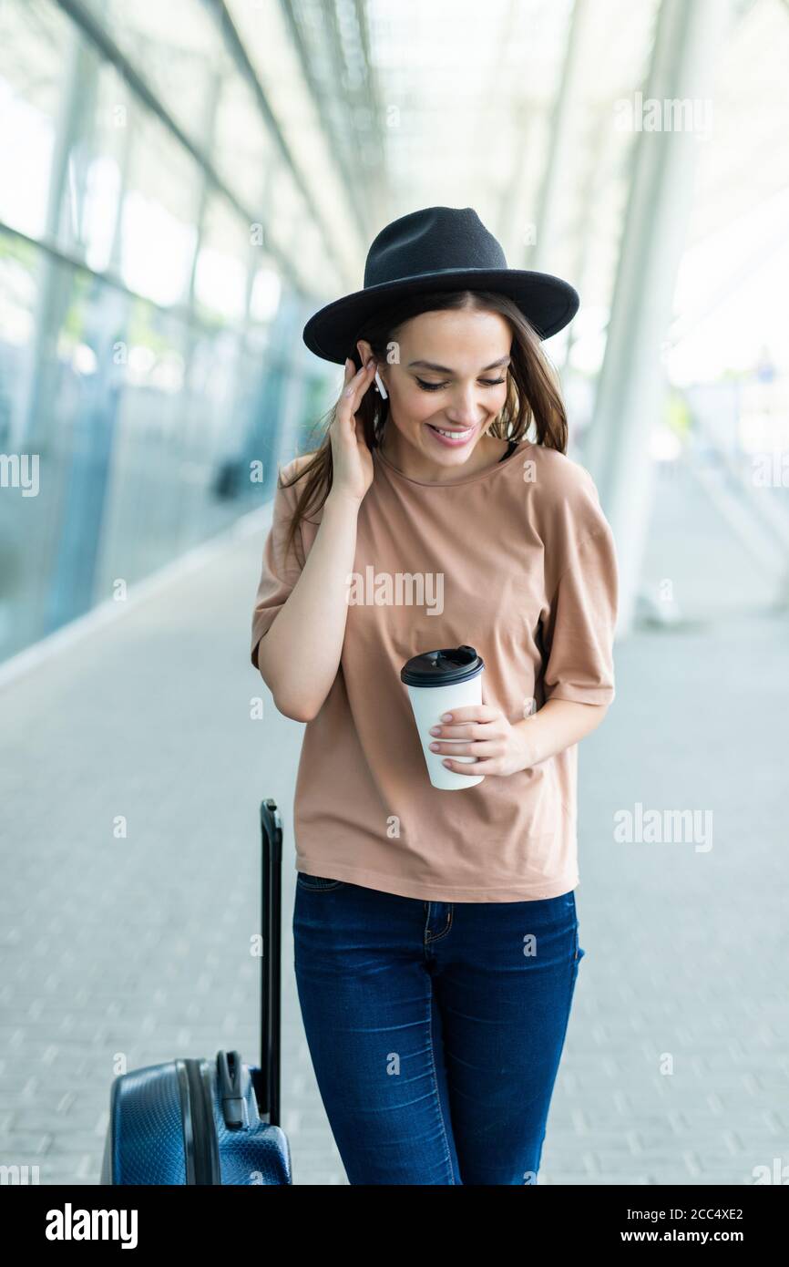 Young woman carry baggage speak via airpods with phone in hands walking to  airport terminal Stock Photo - Alamy