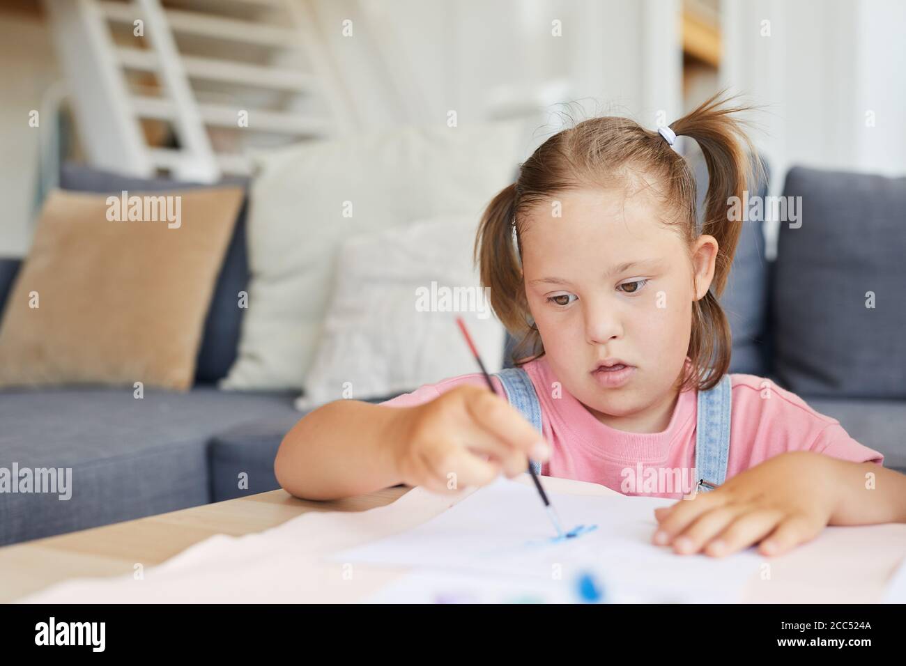Little girl with down syndrome learning to paint with paints at the table at home Stock Photo