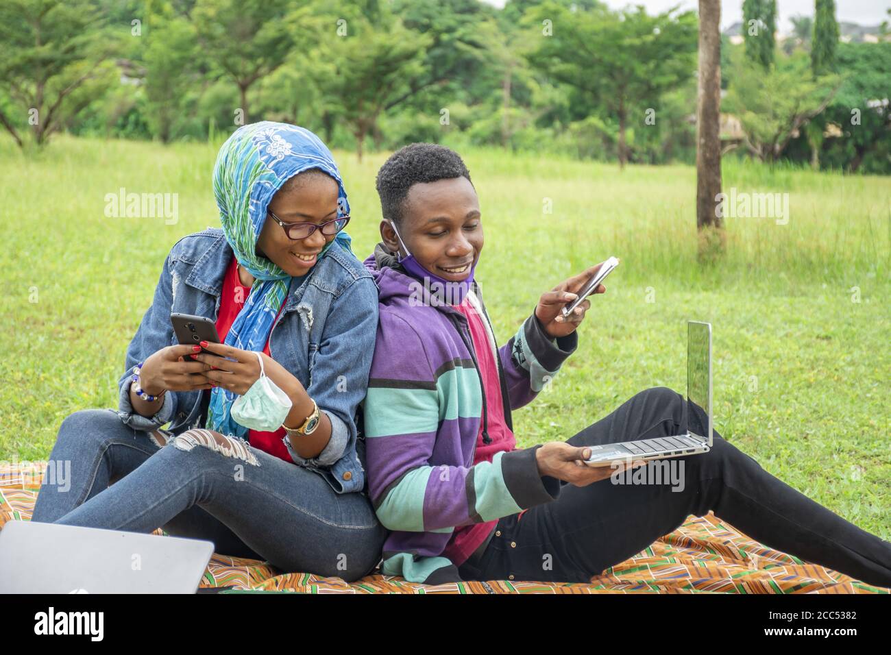 Young African students sitting in a park working on a college task together Stock Photo