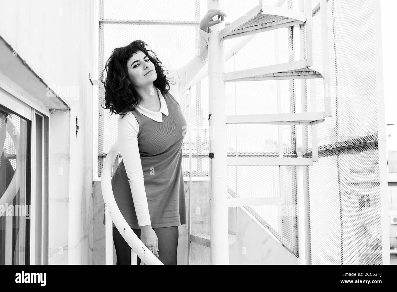 Portrait of a beautiful smiling young woman in an elegant dress standing on a metal stairs. Stock Photo