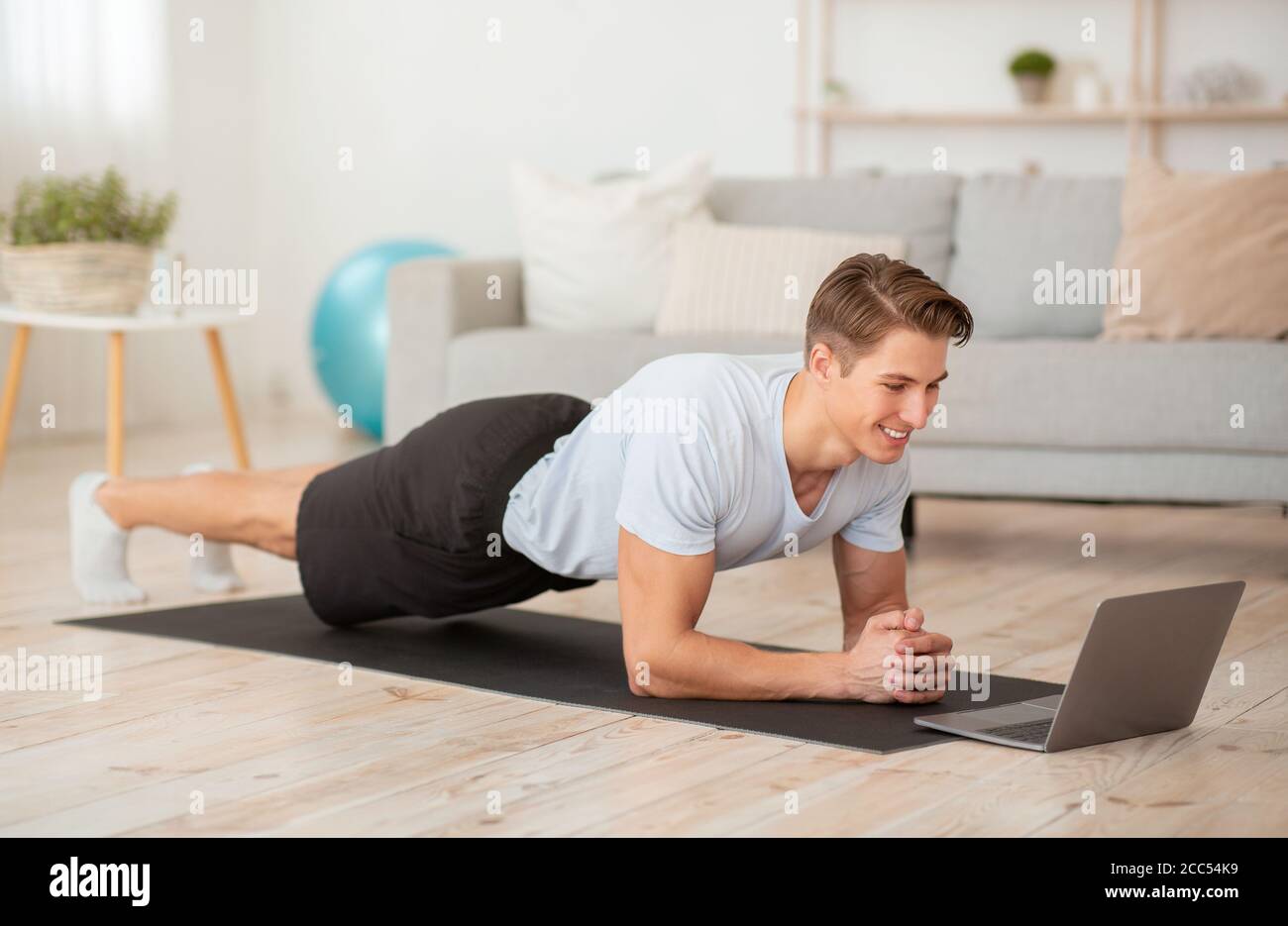 Beautiful body and health care at home during pandemic. Guy watches lesson and makes plank Stock Photo