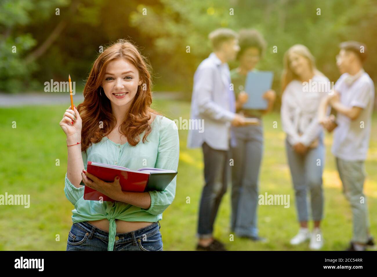 Education Concept. Beautiful nerdy female student and group of her classmates outdoors Stock Photo