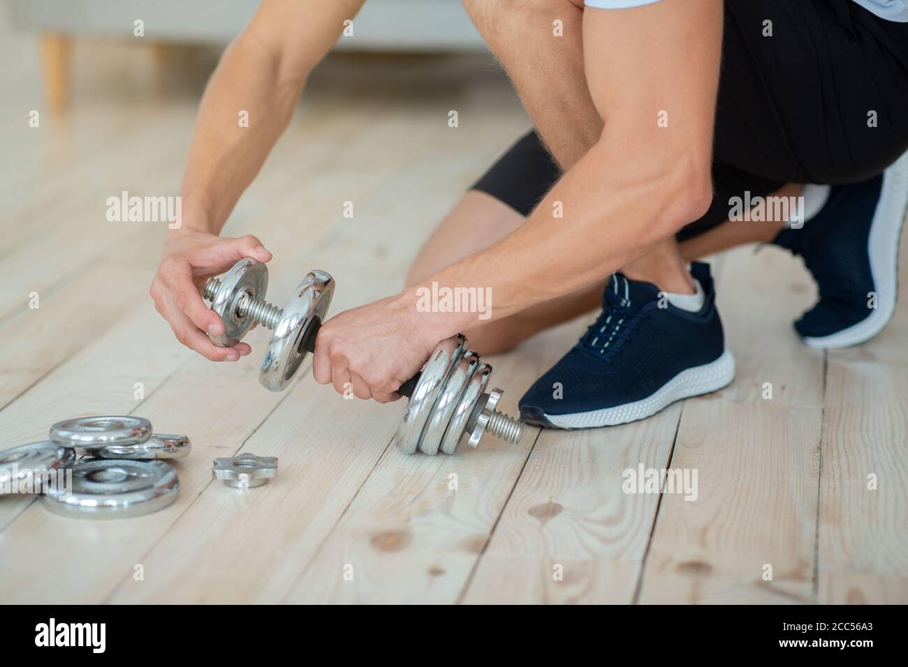 Strength training at home. Man puts discs on dumbbells for workout Stock Photo