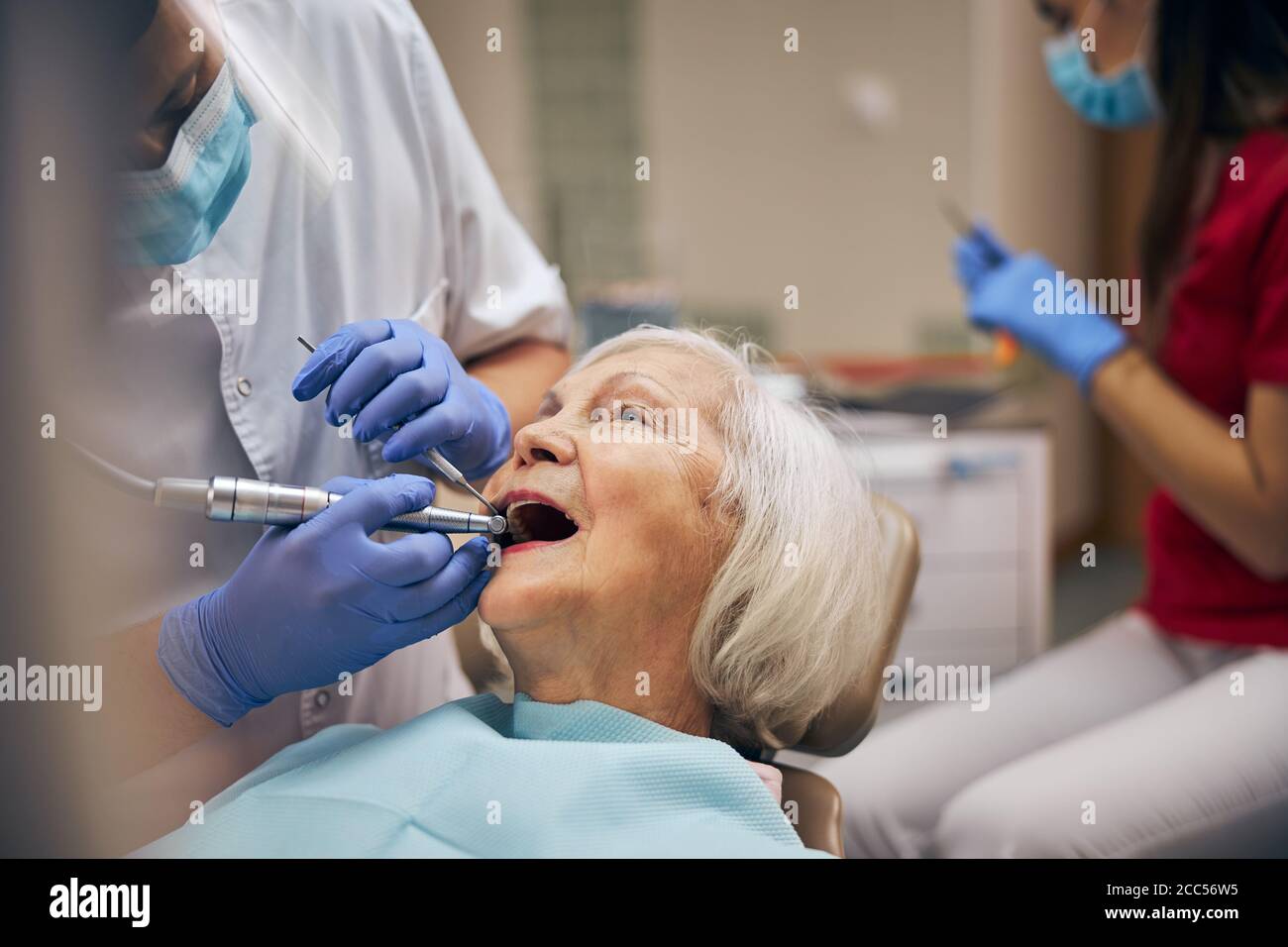 Man dentist with dental tools and drill while caring patient teeth at dental clinic office Stock