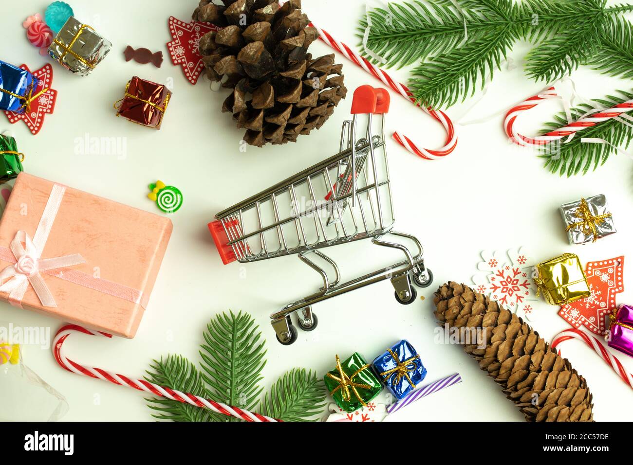 Shopping cart in the center of Christmas decorations on white background. Flat lay. Buying presents on New Year holidays concept Stock Photo