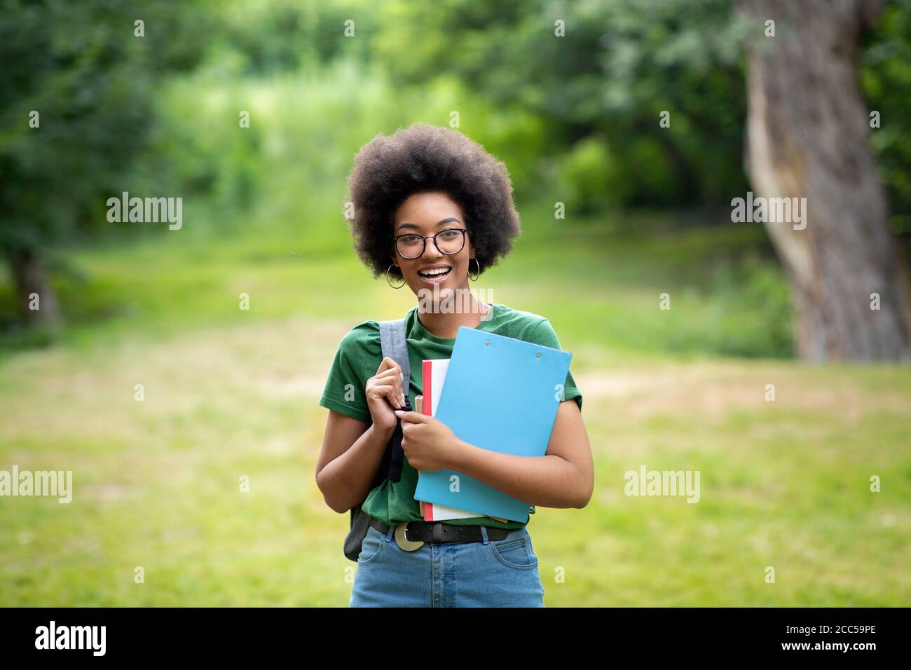 Cheerful Black Female College Student With Backpack And Workbooks Posing Outdoors Stock Photo