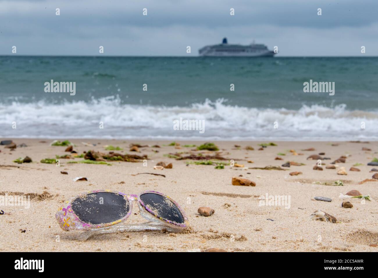 Plastic Pollution: Dropped sunglasses with cruise ship in the background. Bournemouth, UK. Stock Photo