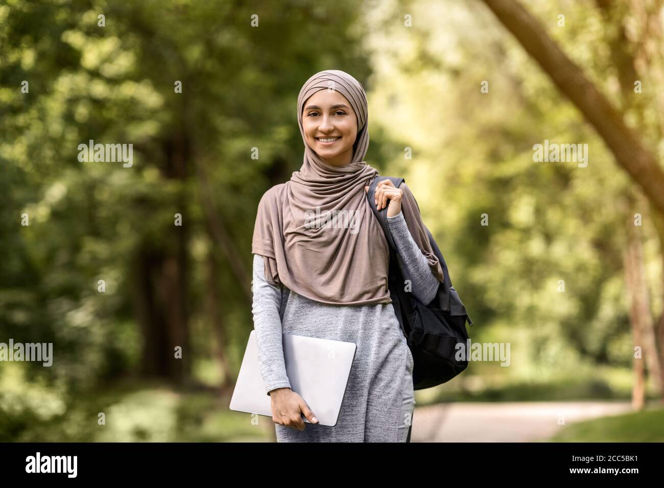 Smiling muslim woman in hijab with laptop posing at park Stock Photo ...