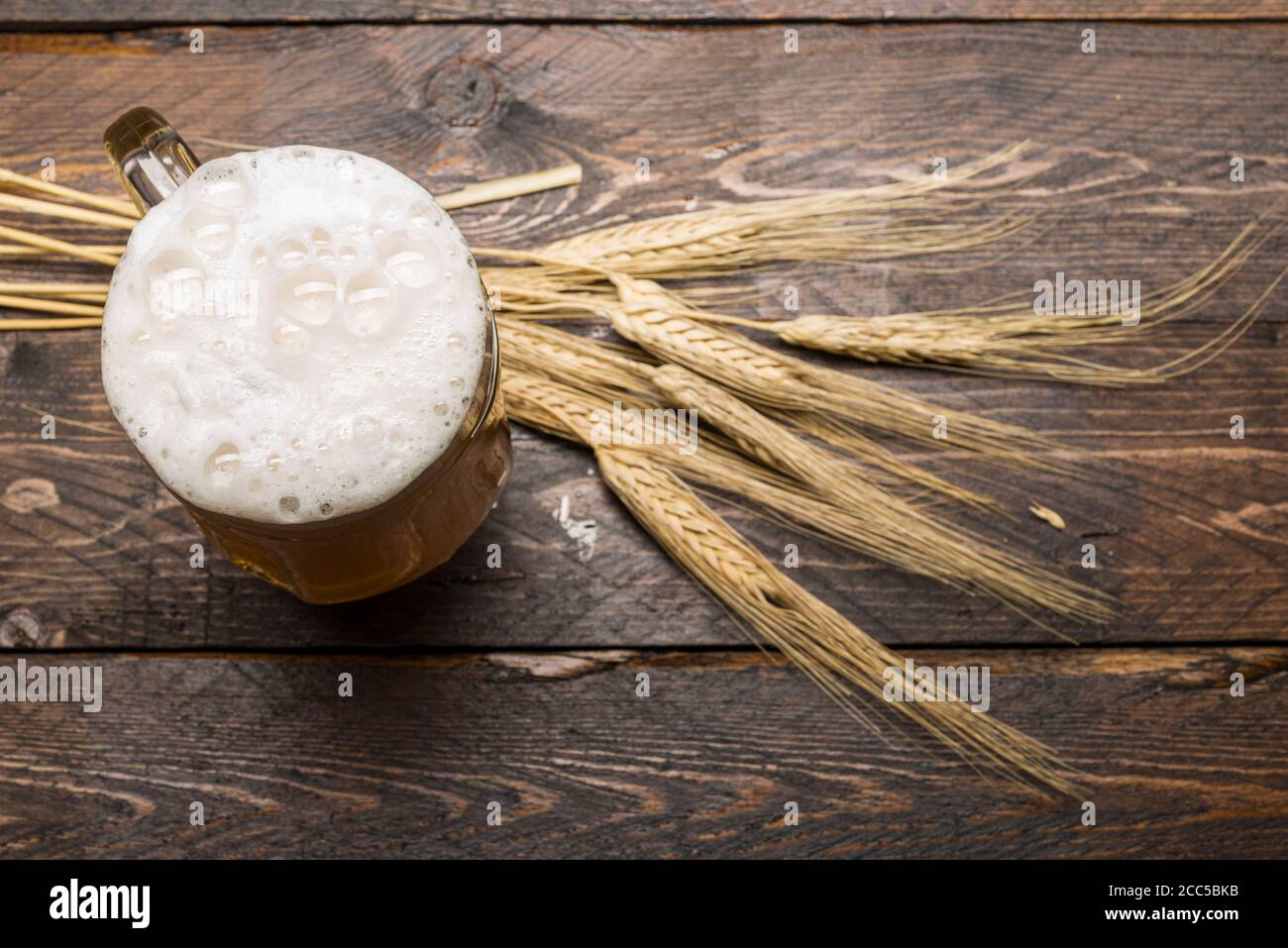 top view of beer pint with foam on wooden table with ears of wheat. Stock Photo