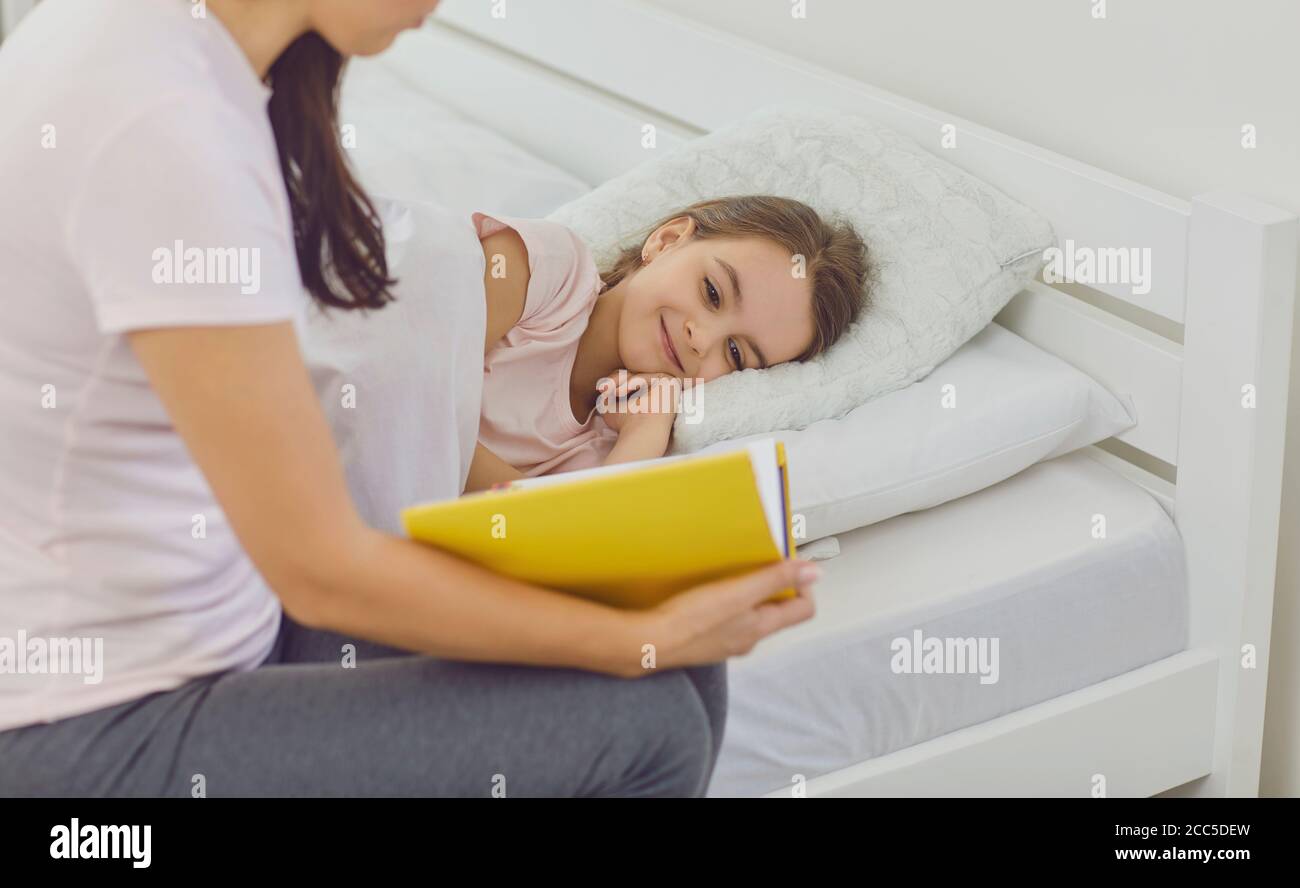Loving mother reading bedtime story to her daughter in bed. Cute girl listening to fairy tale book before sleep Stock Photo