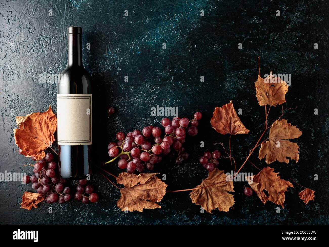 Bottle of red wine with ripe grapes and dried up vine leaves. Old dark ...