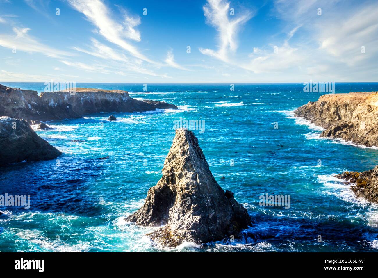 Cone shaped rock in the pacific ocean under a blue sky with clouds ...
