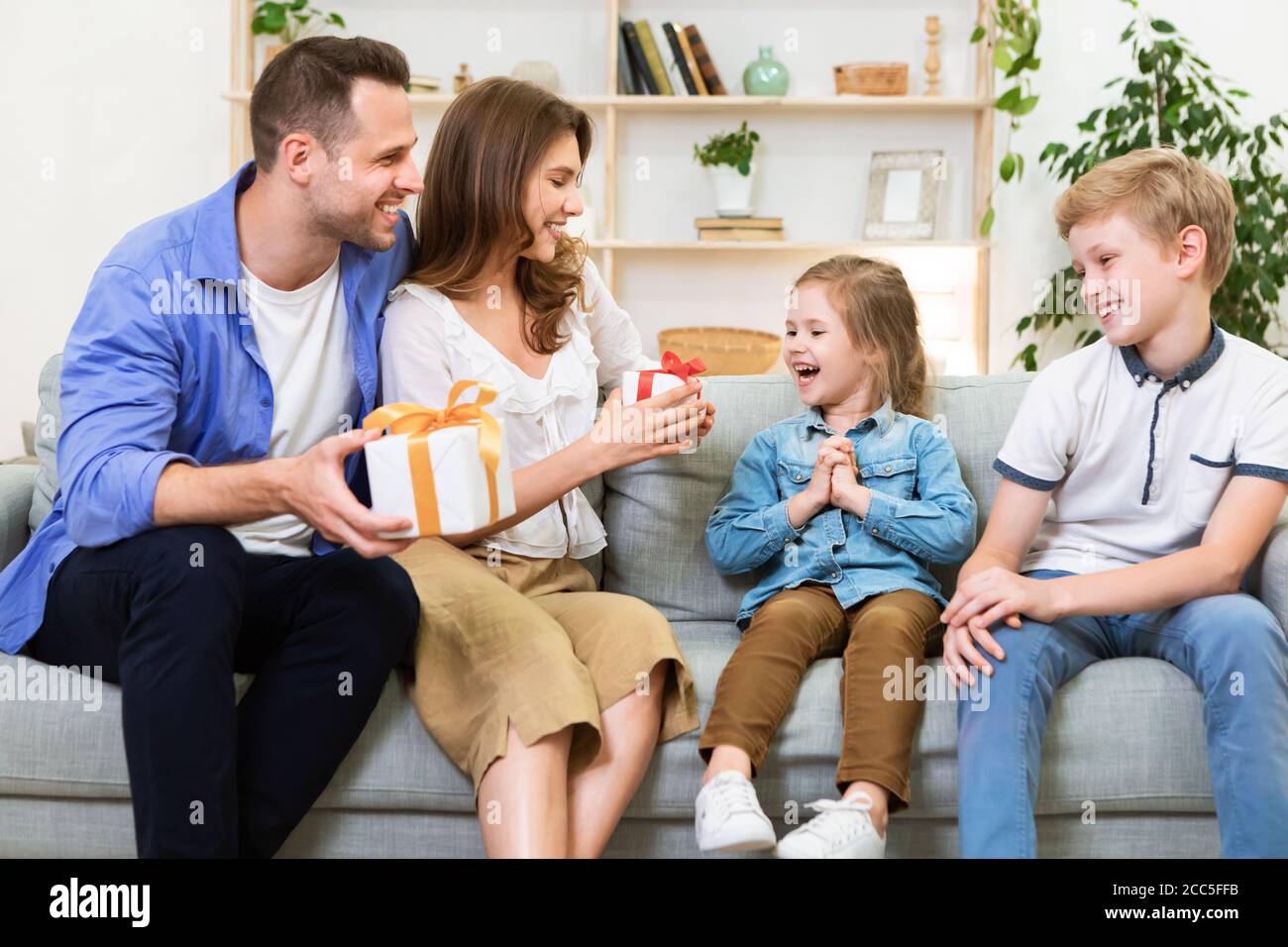 Happy Parents Congratulating Kids Giving Them Gifts Sitting At Home Stock Photo