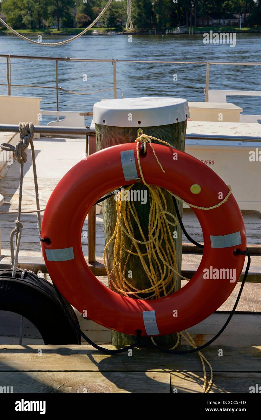 A Coast Guard approved life preserver ring in international orange color stands ready in a life ring station attached to a dock piling. Stock Photo
