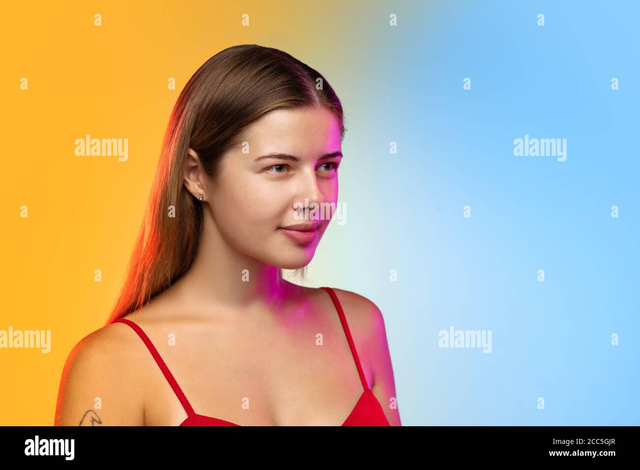 Suspecting. Close up caucasian young woman's portrait on gradient studio background in neon. Beautiful female model in casual style. Concept of human emotions, facial expression, youth, sales, ad. Stock Photo