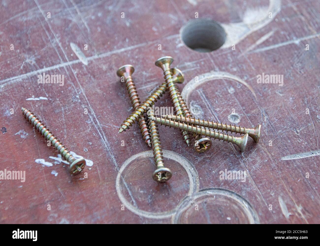 Pile of screws on a cut up wooden work bench being used for home improvements Stock Photo