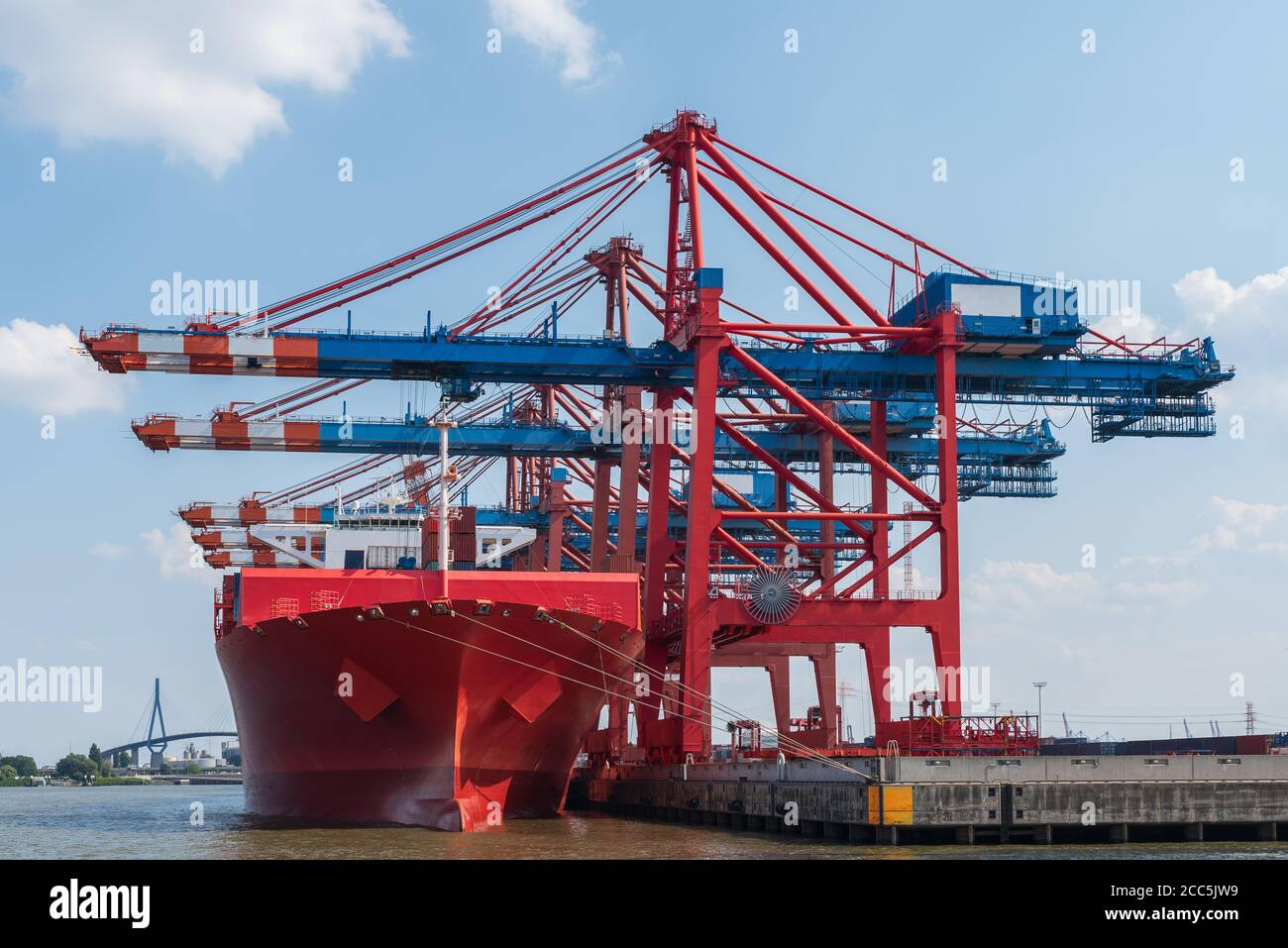 waterside view of container ship and gantry cranes at commercial dock against blue sky Stock Photo