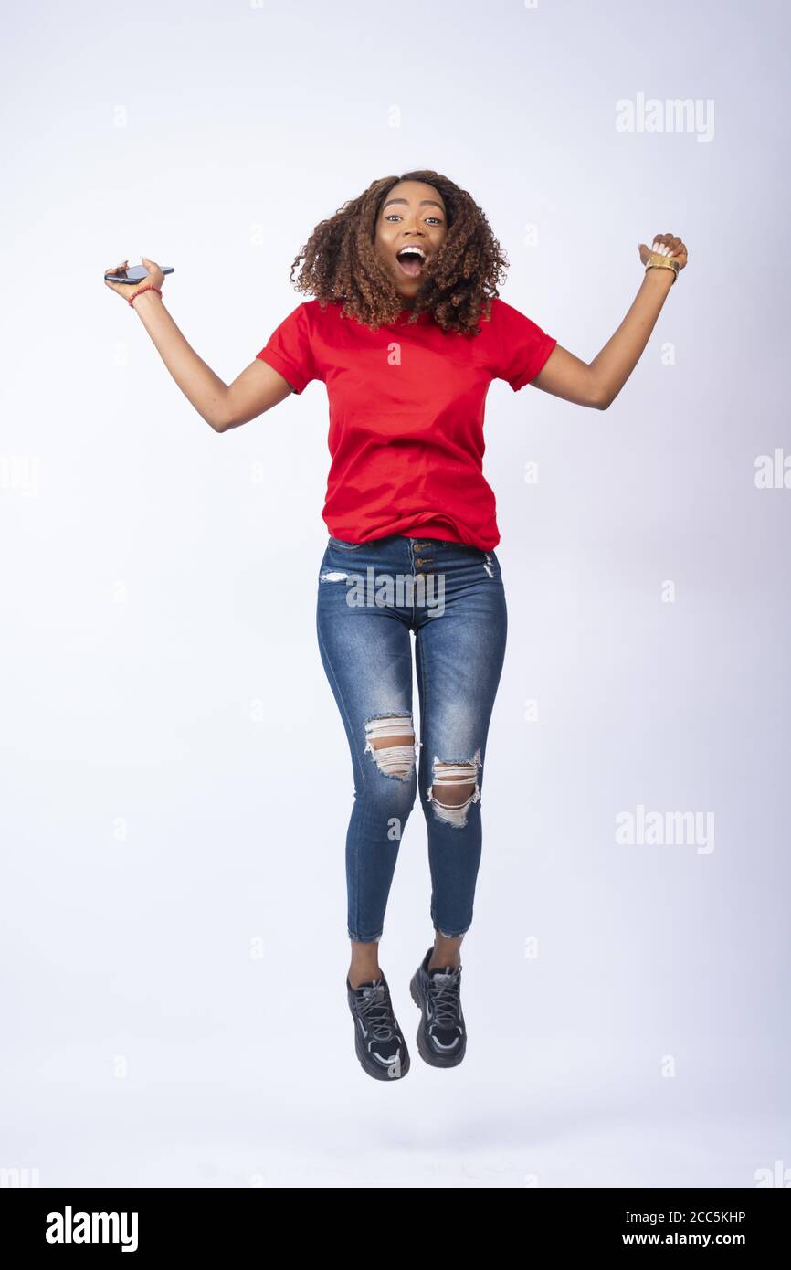 happy young african lady jumping in excitement, holding her phone Stock Photo
