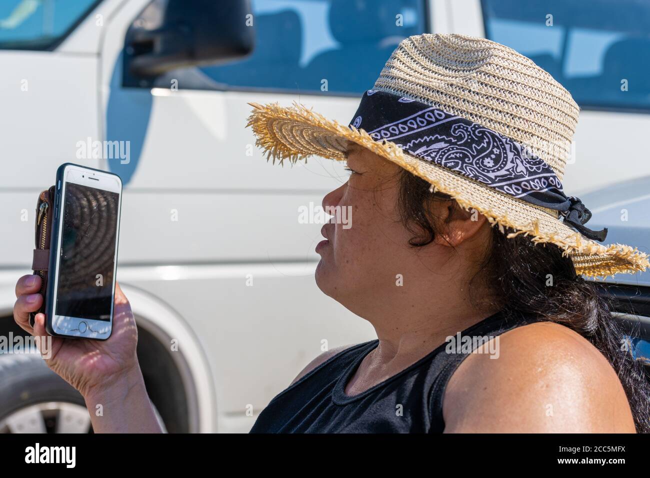 Closeup picture of a middle-aged Asian woman with a straw hat speaking in a smartphone a hot summer day. Bright blue sky in the background Stock Photo