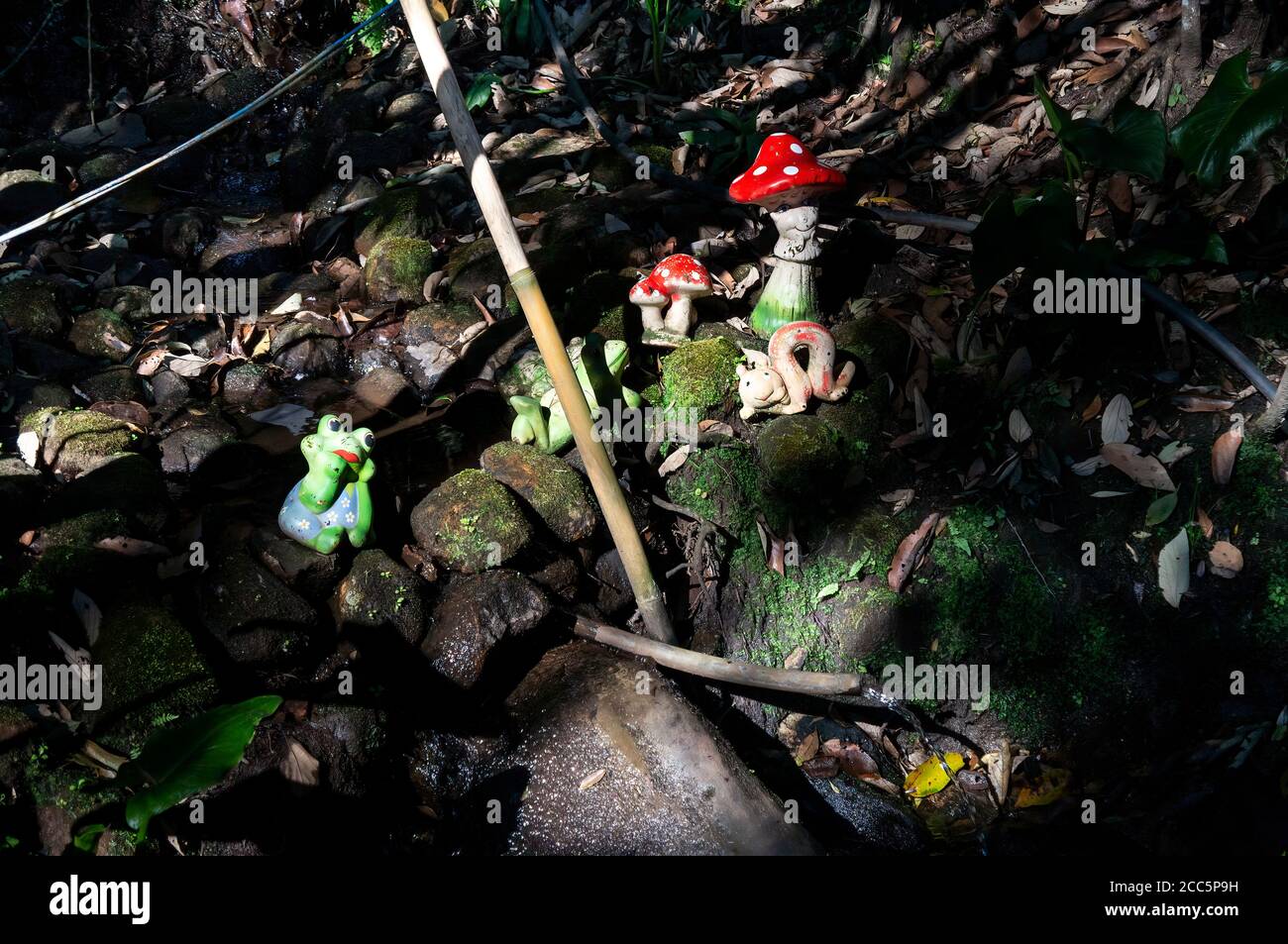 Garden ornaments over some rocks and close to a stream of crystal clear water under tree shade found inside O Contemplario farm. Stock Photo