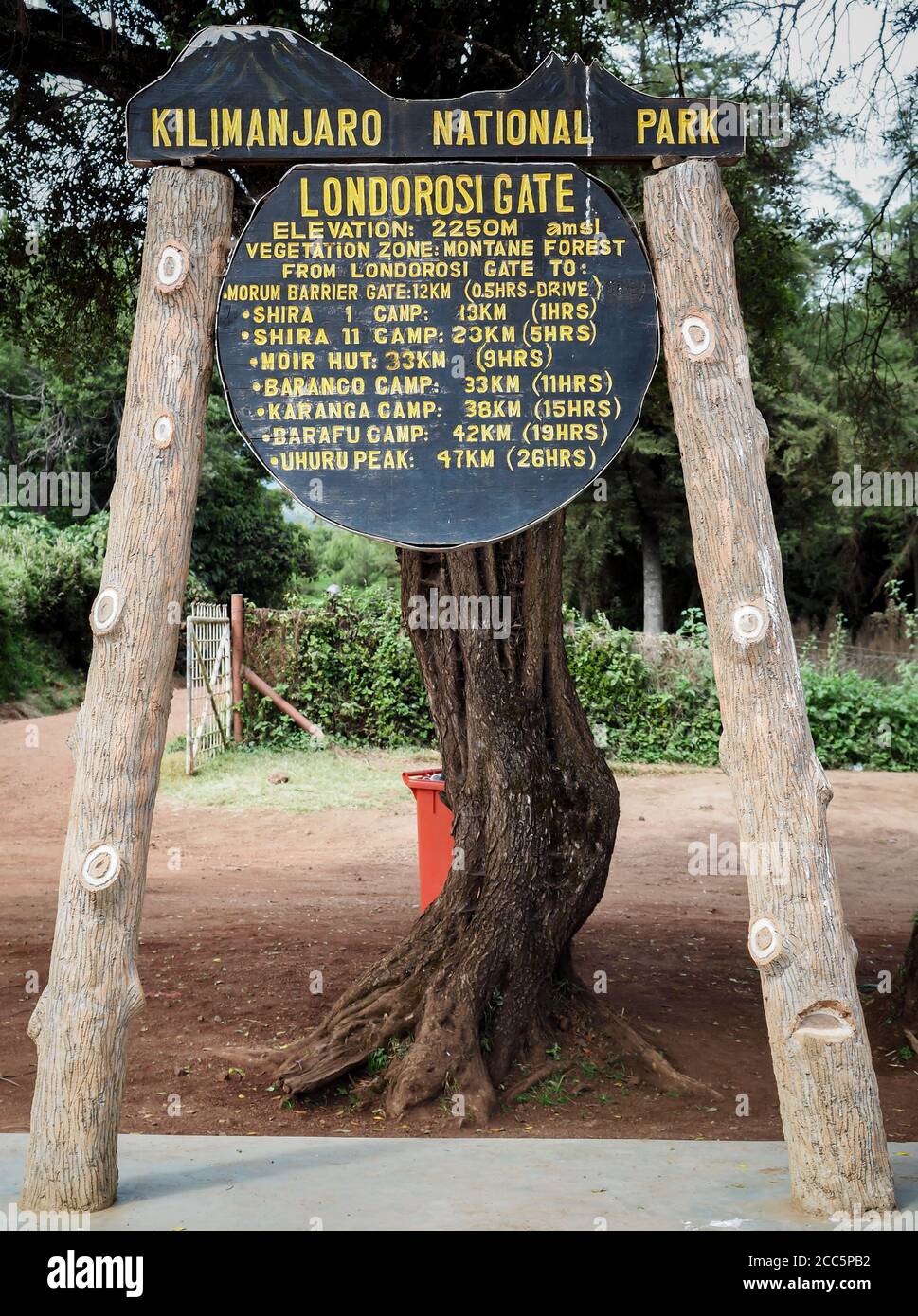 the base camp sign post. guides porters and sherpas carry heavy sacks as they ascend mount kilimanjaro Stock Photo