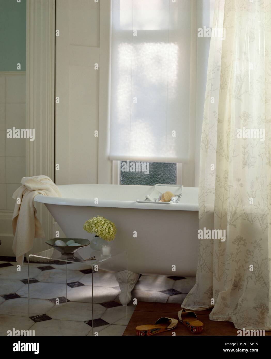 A traditional roll-top bath in allwhite bathroom with voile curtain and ...