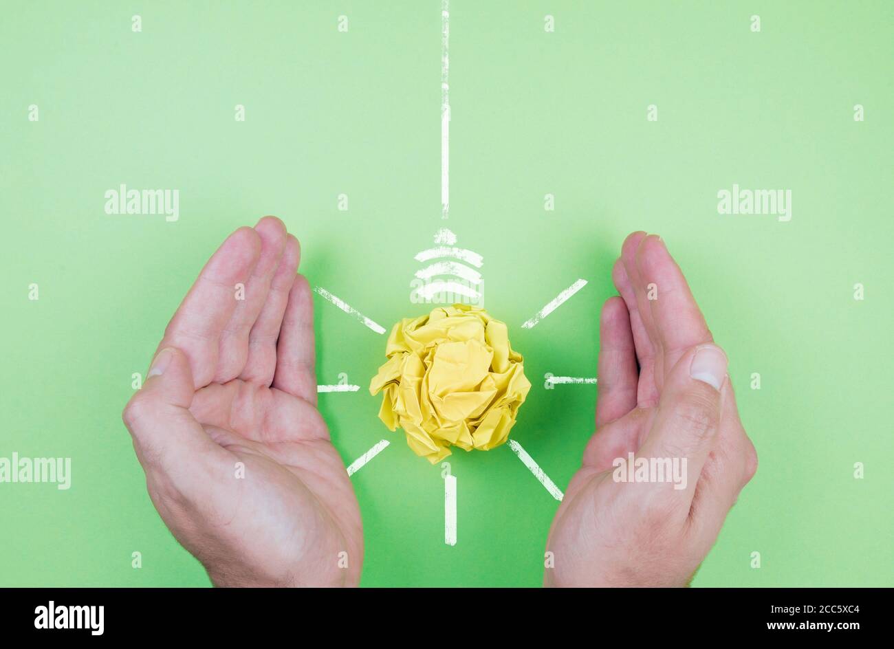 energy conservation and sustainability concept, hands shielding yellow paper light bulb on green background Stock Photo