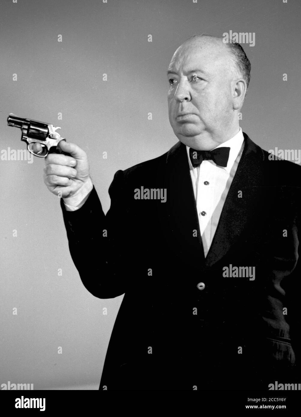 Publicity photo of film and television director Alfred Hitchcock  wearing a tuxedo, as he aims a pistol revolver for his anthology television series, 'The Alfred Hitchcock Hour,' 1962, CBS.  File Reference # 34000-246THA Stock Photo