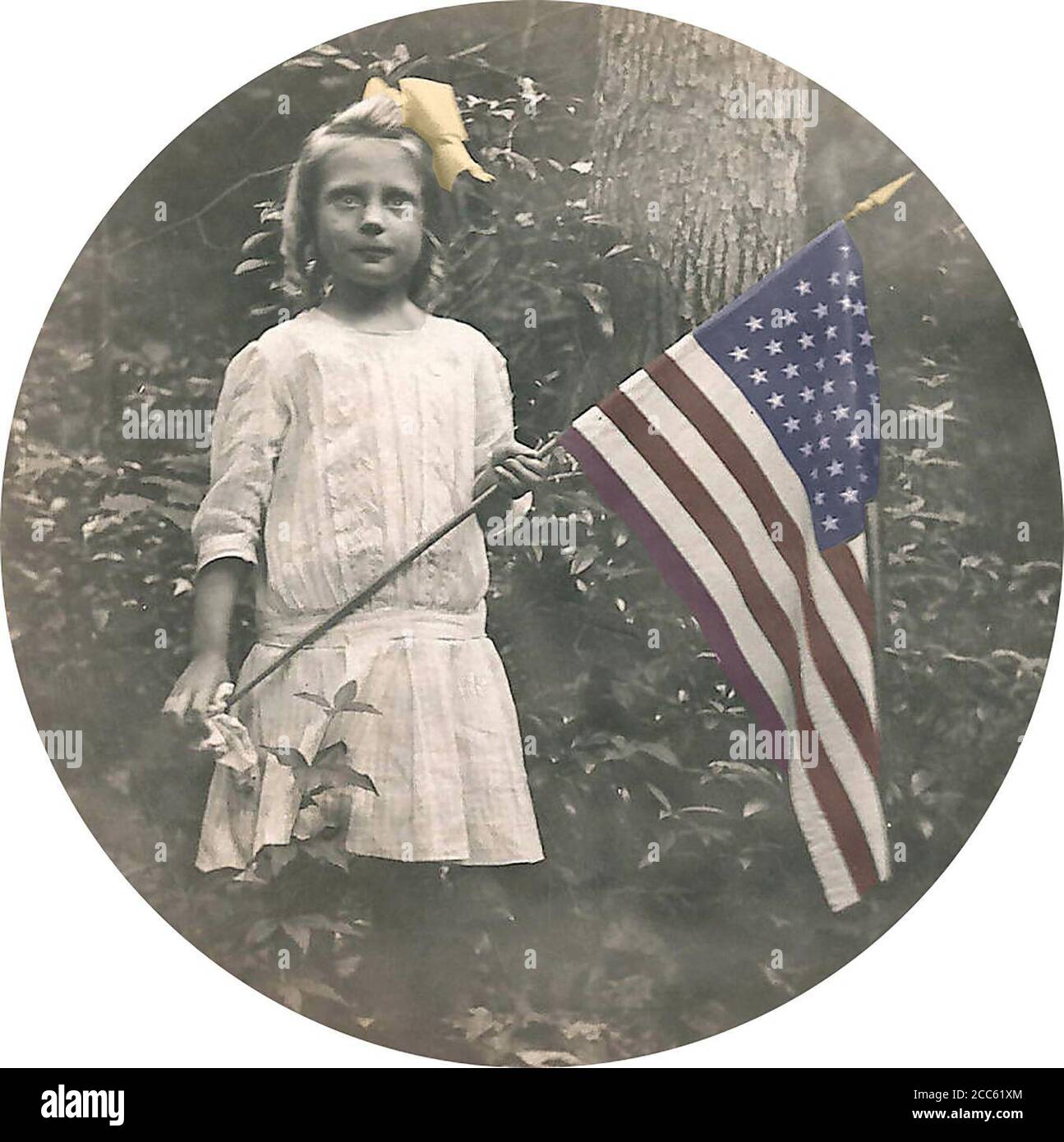 A serious little girl stands with US Flag - 48 stars.  1904-1918; colorized Stock Photo