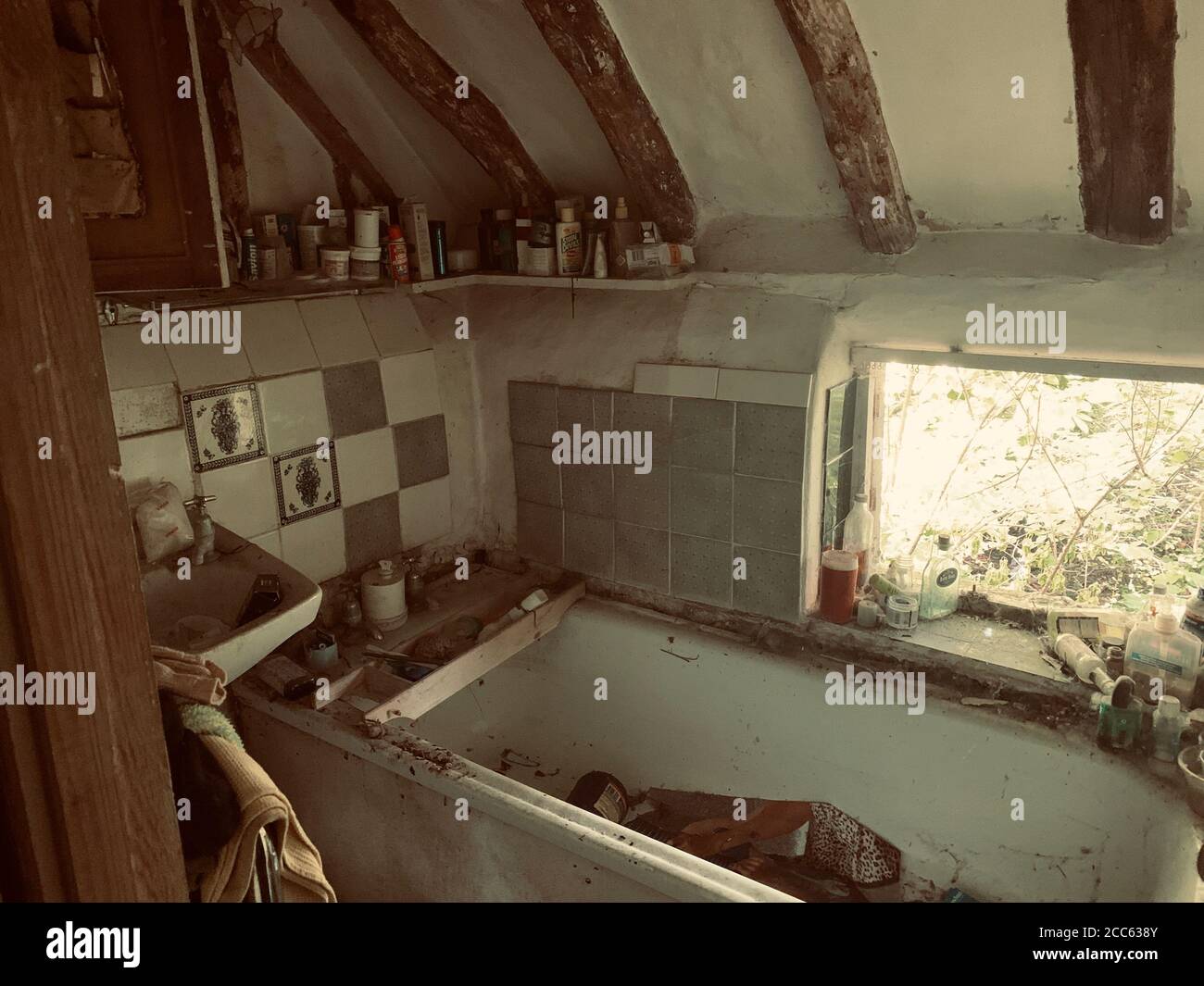A grimy bath, with what was once a lovely window view. UK: CHILLING images of an abandoned cottage with a collection of empty Marmite bottles have bee Stock Photo