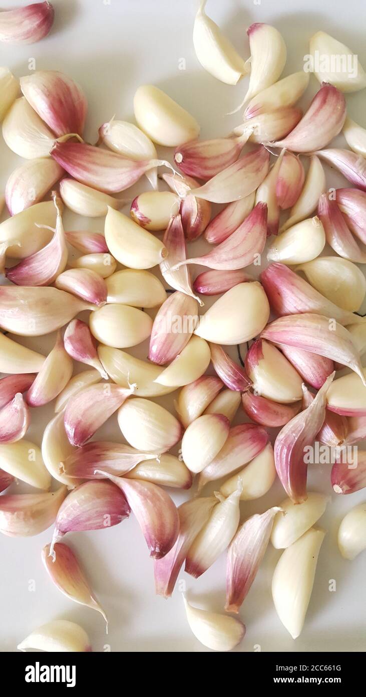 Lots of fresh juicy red-white garlic cloves on white ceramic background  in top view image. Stock Photo