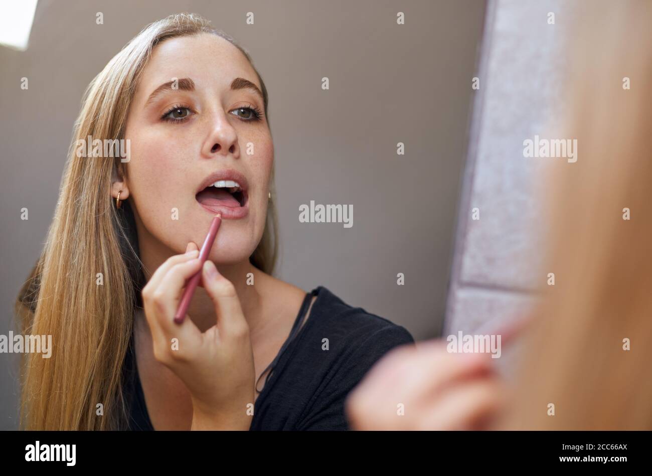 Young blonde woman applying makeup in mirror in bathroom Stock Photo