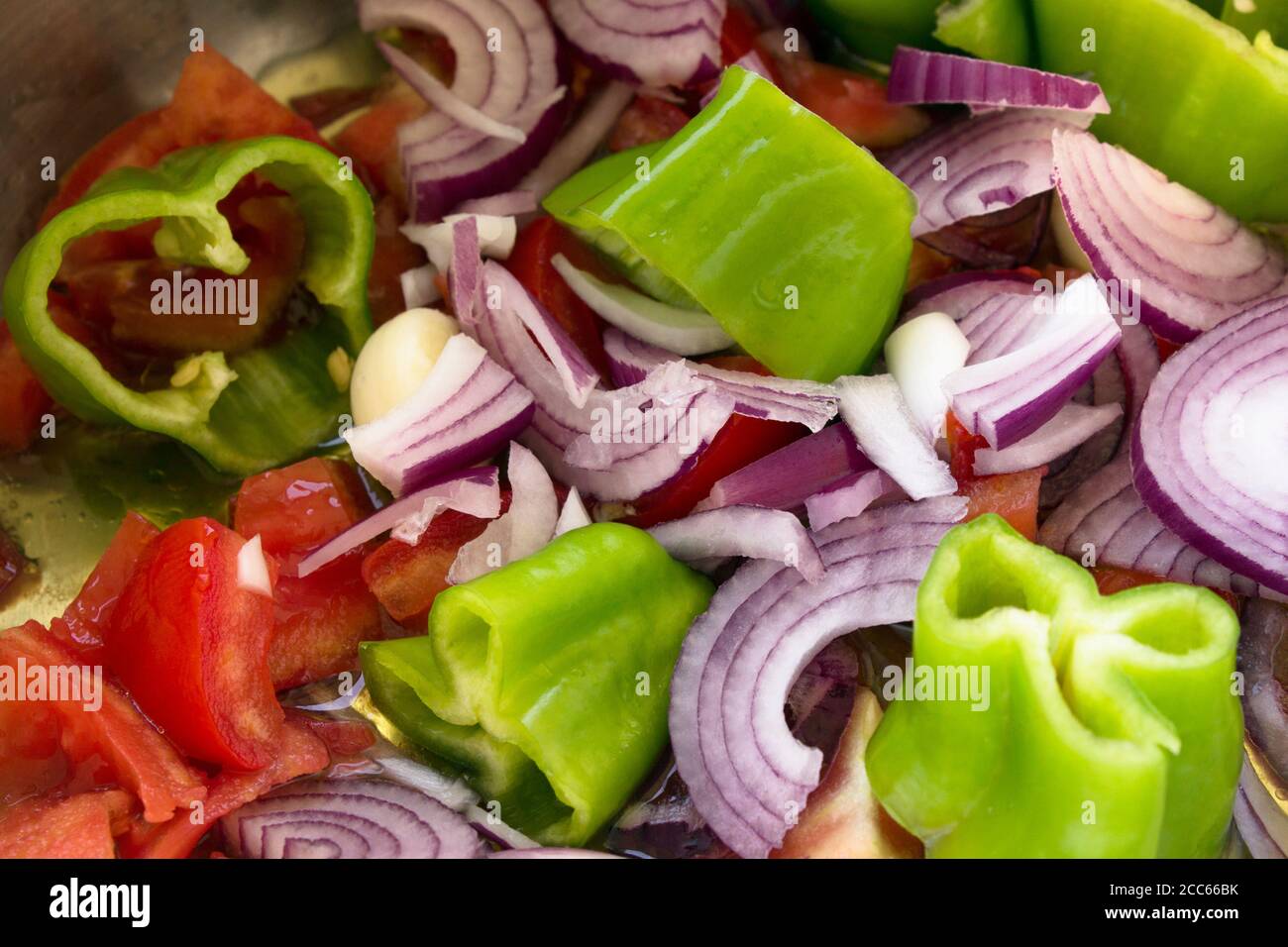 Close up of sliced red and green peppers and red onions with garlic to be cooked with olive oil. Stock Photo