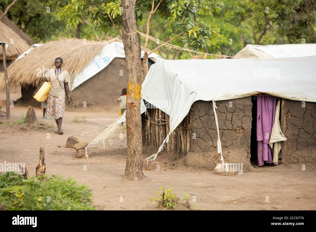 Refugees from South Sudan live in makeshift mud and grass thatch homes covered in tarpaulin sheets in Palabek Refugee Settlement in northern Uganda, East Africa. Stock Photo