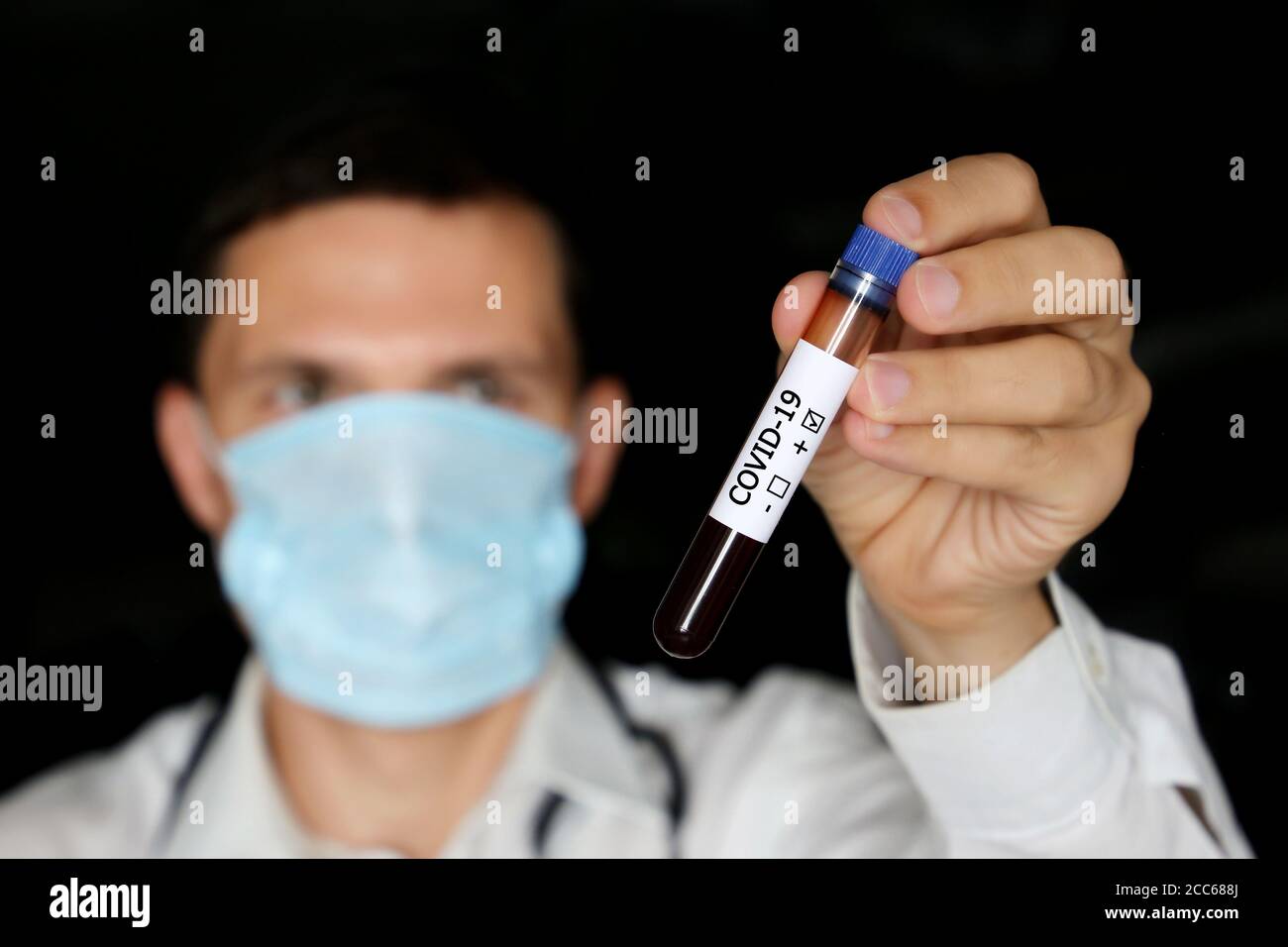 Test tube with covid-19 blood sample in male hand close up, man in medical mask holding a vial. Doctor or scientist with positive coronavirus test Stock Photo