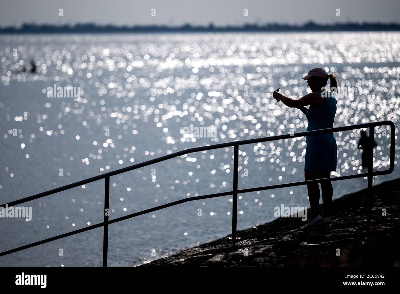 Wilhelmshaven, Germany. 19th Aug, 2020. A woman stands in the back light and takes photos on the south beach. Credit: Sina Schuldt/dpa/Alamy Live News Stock Photo