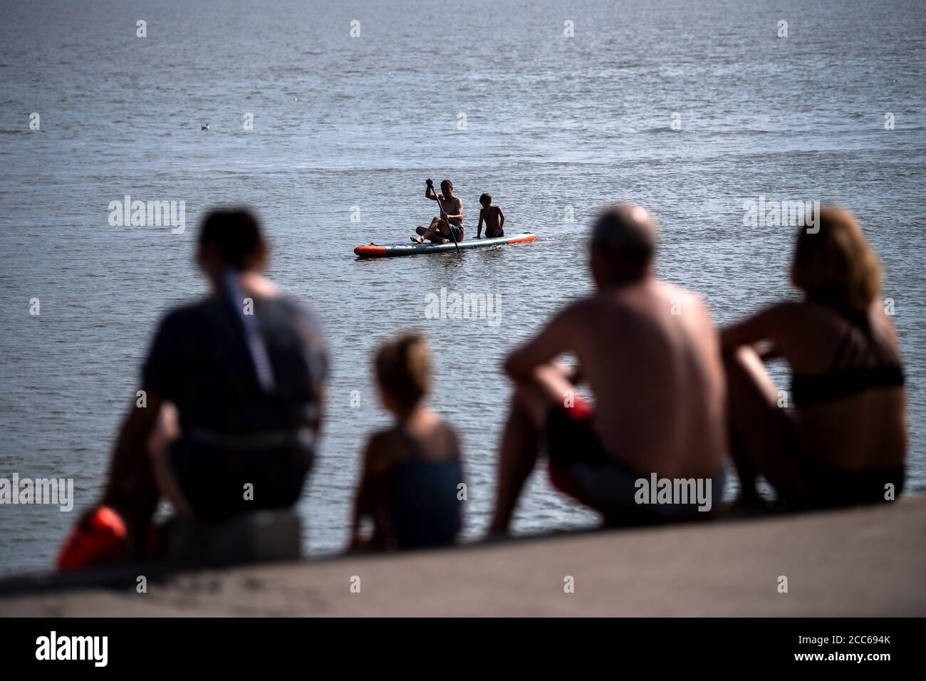 Wilhelmshaven, Germany. 19th Aug, 2020. Visitors watch two people paddling past on a Stand Up Paddling (SUP) Board on the south beach. Credit: Sina Schuldt/dpa/Alamy Live News Stock Photo
