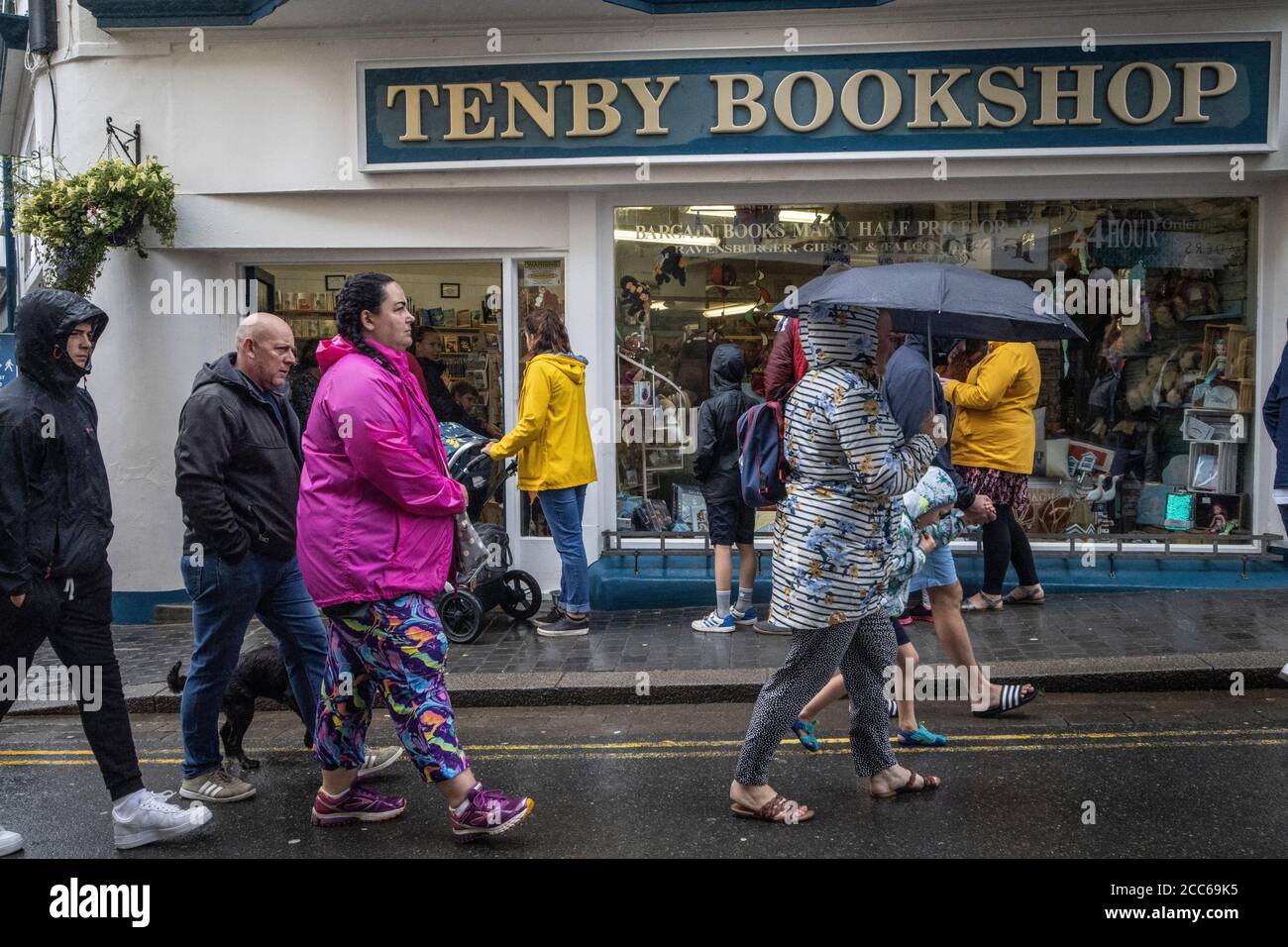Tenby, West Wales. 19th Aug 2020. UK Weather: Tourists queue in the rain outside a bookshop on the high street at Tenby looking for alternative things to do. During the post-lockdown tourists have found a lot of attractions still closed to visitors in West Wales. Storms and bad weather hit South England and West Wales during the night and continued into the day keeping tourists off the beaches across Pembrokeshire, United Kingdom. Wednesday 19th August 2020. Tenby, Pembrokeshire, West Wales, UK Credit: Jeff Gilbert/Alamy Live News Stock Photo