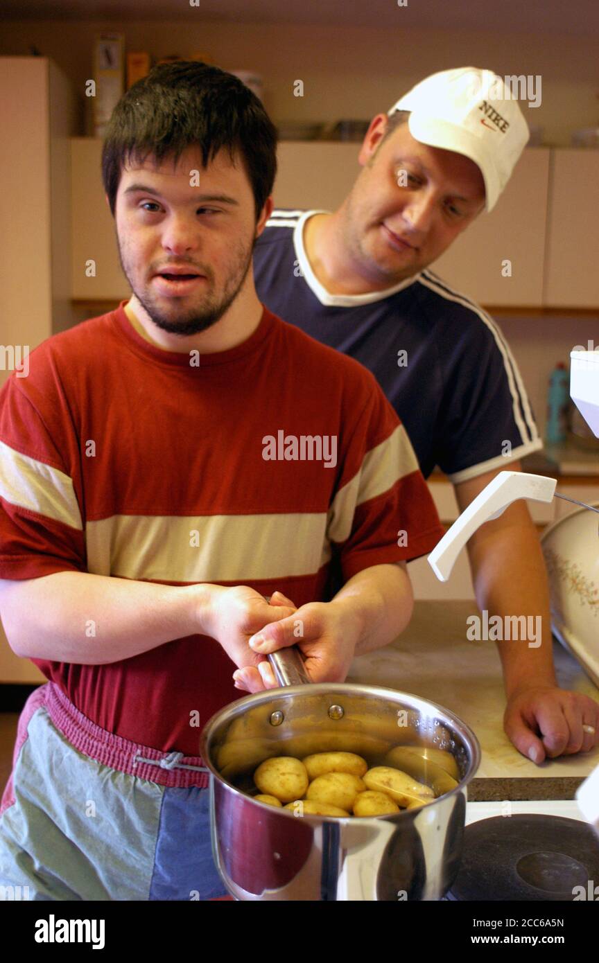 Young man with learning disability living in sheltered housing scheme; making his own meal with support worker in kitchen; UK Stock Photo