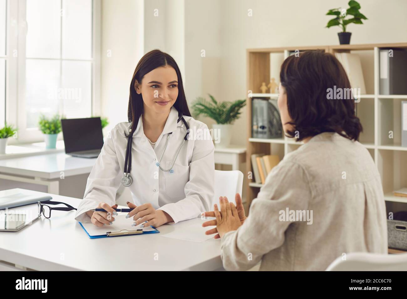 Young smiling doctor therapist listening to patients complaints and making notes in clinic Stock Photo