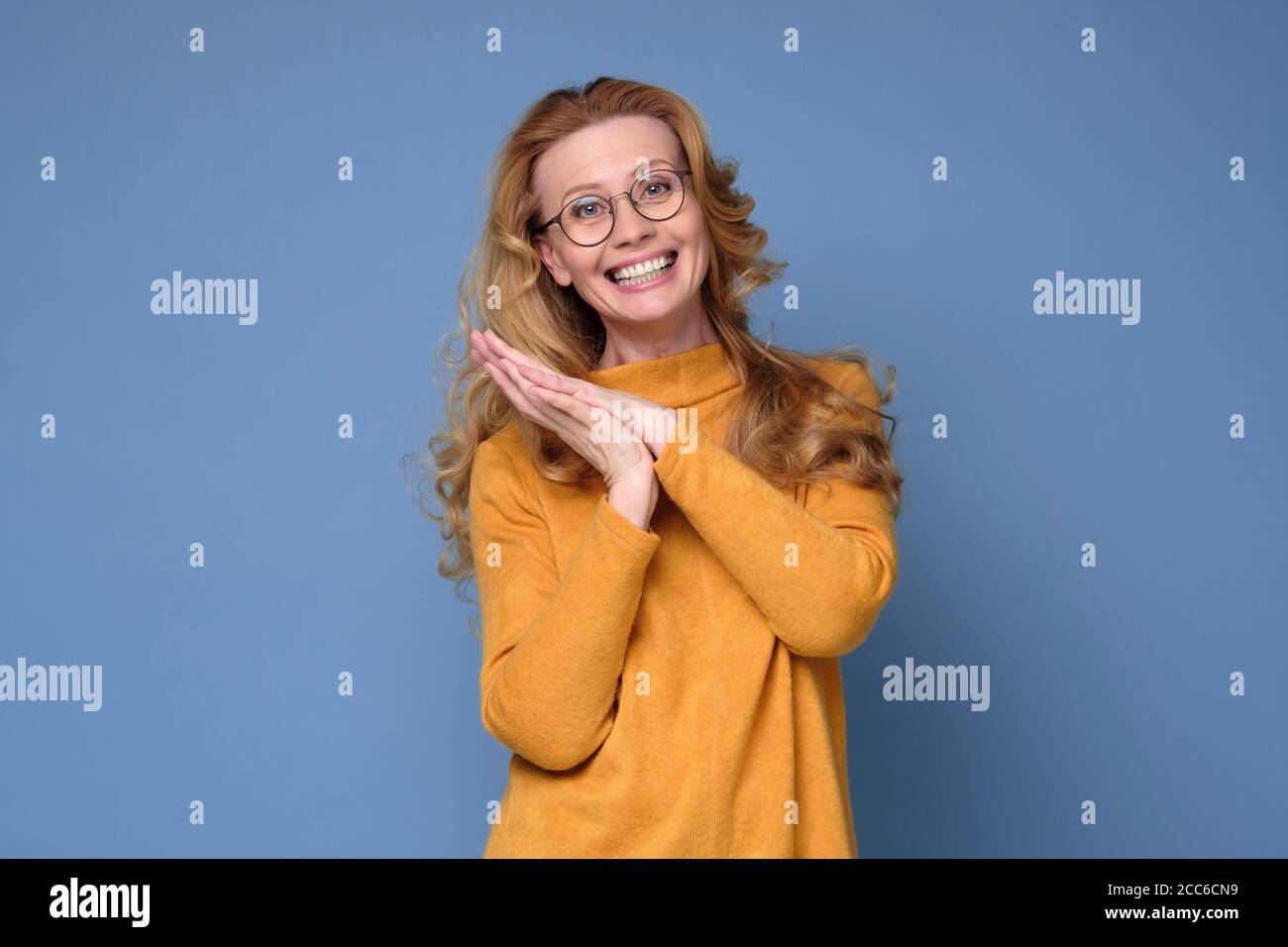 Woman looking at camera and smiling while standing against blue background. Stock Photo