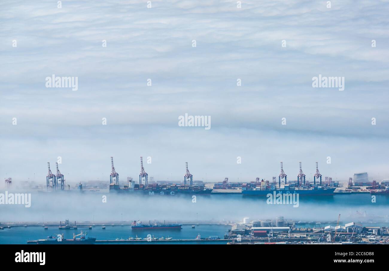 Cranes towering above sea fog seen from above in the distance, Cape Town harbour, South Africa Stock Photo