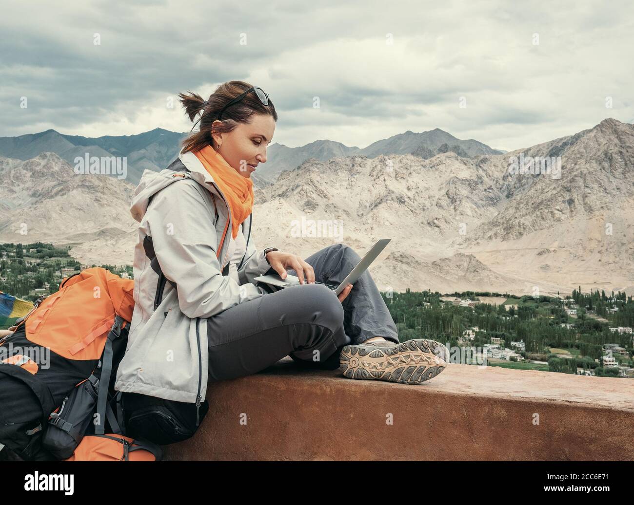 Backpacker with laptop sits on the top view point under mountain settelment Stock Photo