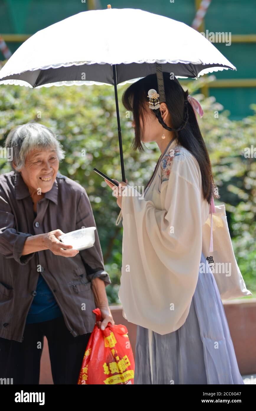 Wuhan: A chinese old lady begs for money to a young girl dressed on traditional clothes, in Jianghan Road. China Stock Photo