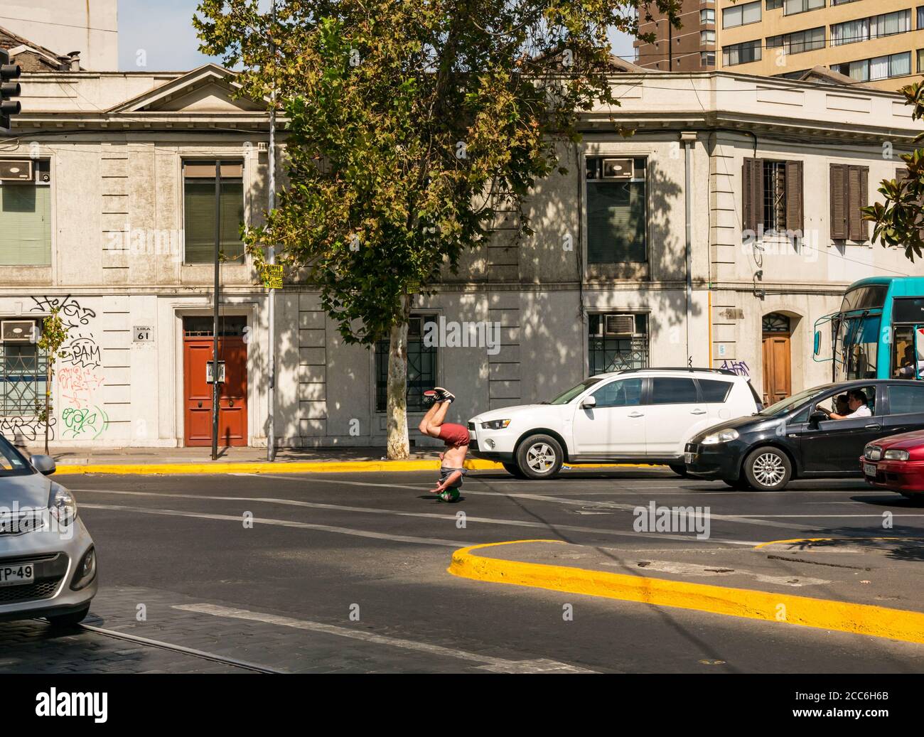Street performer wearing helmet twirling on head at road junction with traffic stopped at lights hoping for money, Santiago, Chile, South America Stock Photo